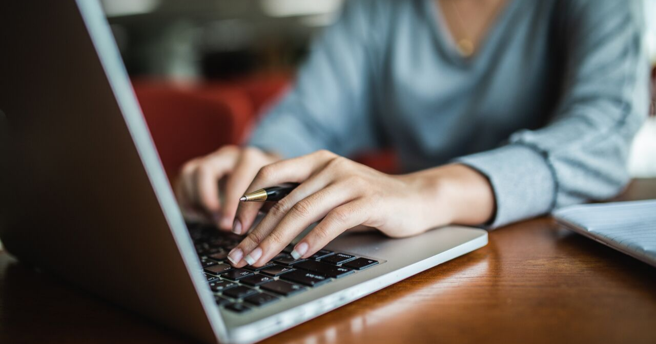 A woman holds a pen and types on a laptop