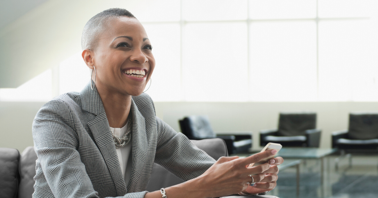 A woman in a suit holds her phone and smiles