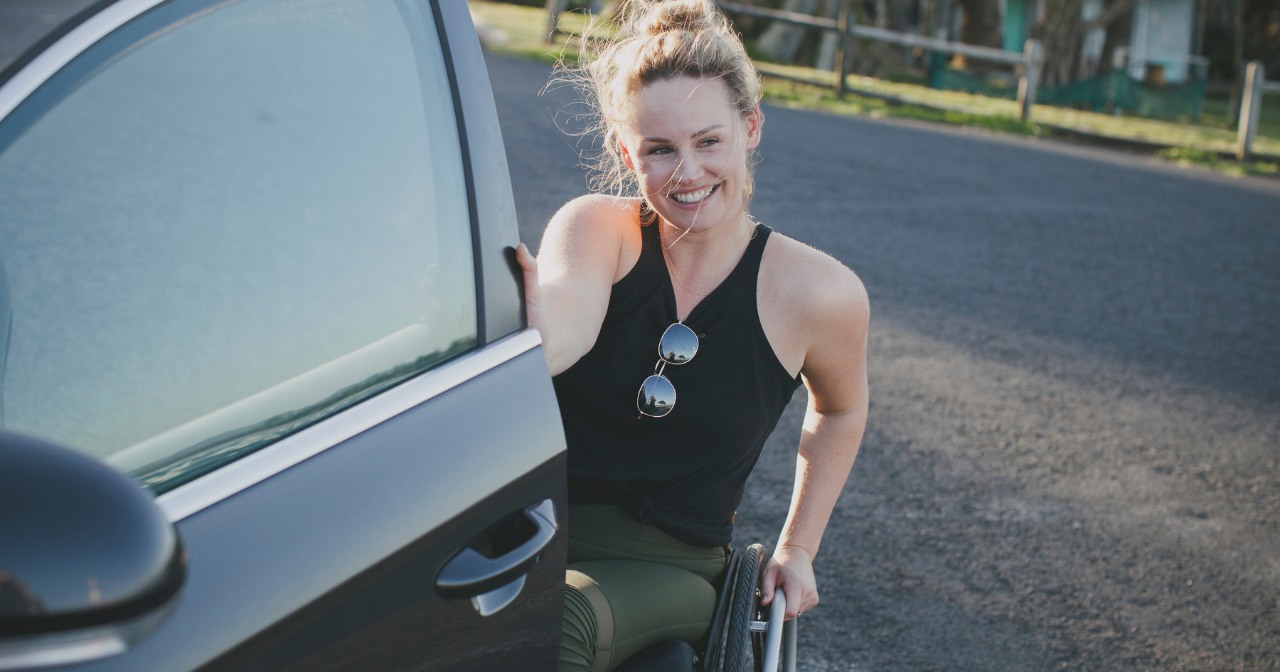 A woman in a wheelchair smiles while opening her car door. 