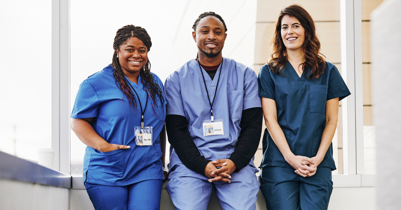 Three health care providers sit on a half wall and smile for a photo. 