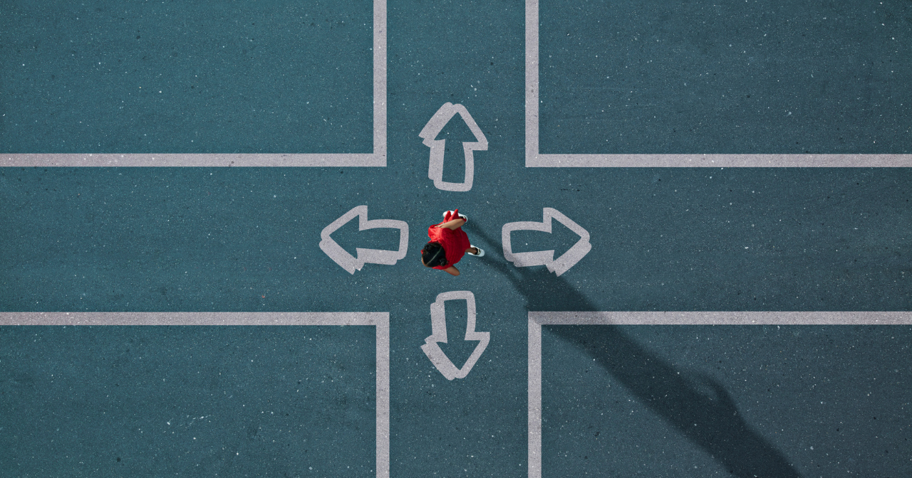 An overhead photo of a woman dressed in red stands in the middle of a painted intersection deciding which way to go. 