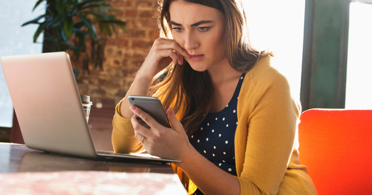 A woman bites at her nails while looking, concerned, at her phone. 