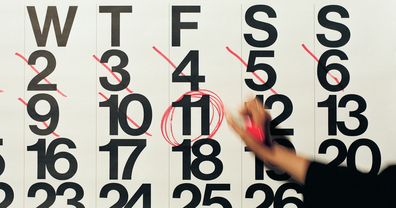 A hand holding a red marker is circling a date on a calendar. 