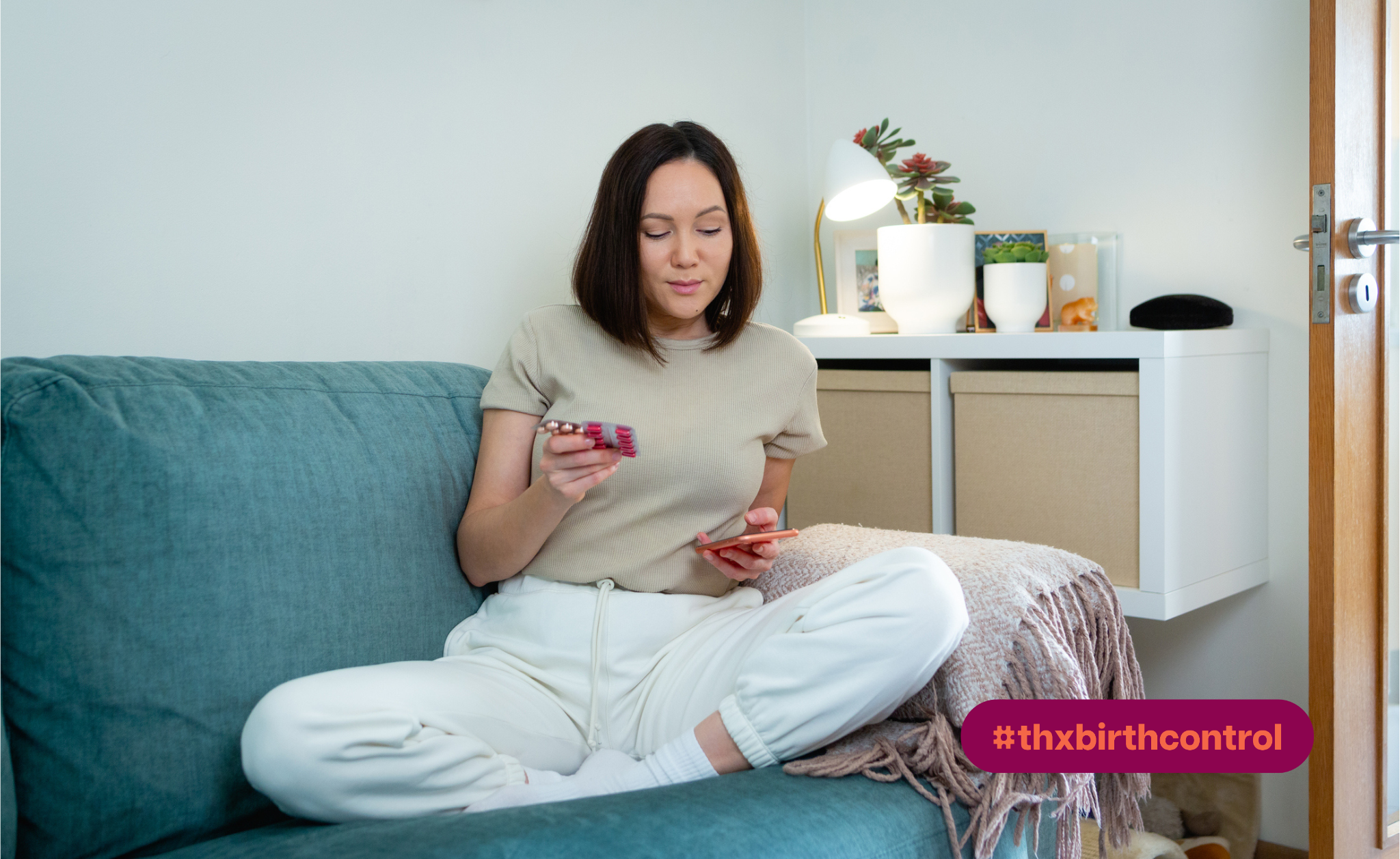 Woman looking at contraceptives and her phone while sitting on the couch.