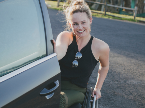 A woman in a wheelchair smiles while opening her car door. 