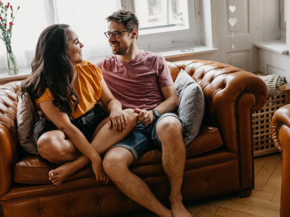 A heterosexual couple sits on a sofa and chats. 