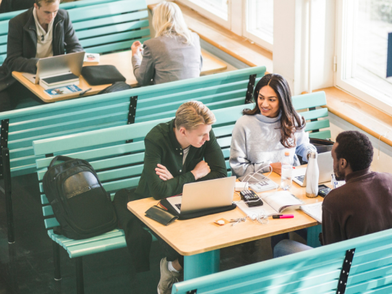 Three college students sit at a table together and do schoolwork. 