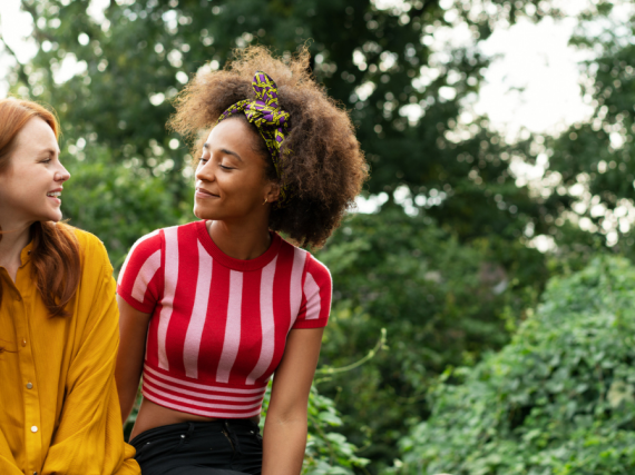 Two friends sit on a wall next to one another and share a smile. 