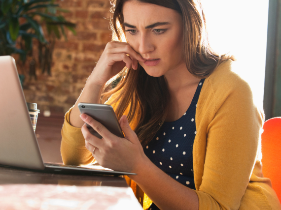 A woman bites at her nails while looking, concerned, at her phone. 