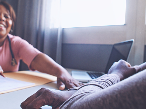 A female provider and patient laugh together while sitting across from each other at a table. 