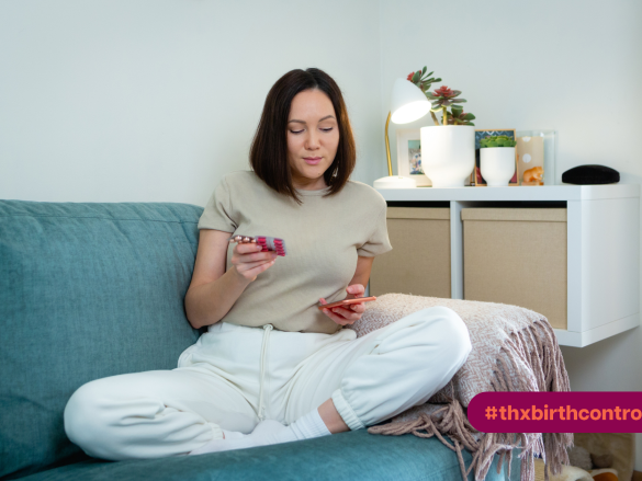 Woman looking at contraceptives and her phone while sitting on the couch.